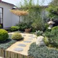 Small Japanese garden courtyard with curved stepping-stone path, stone lantern, bamboo backdrop, and mossy groundcovers.