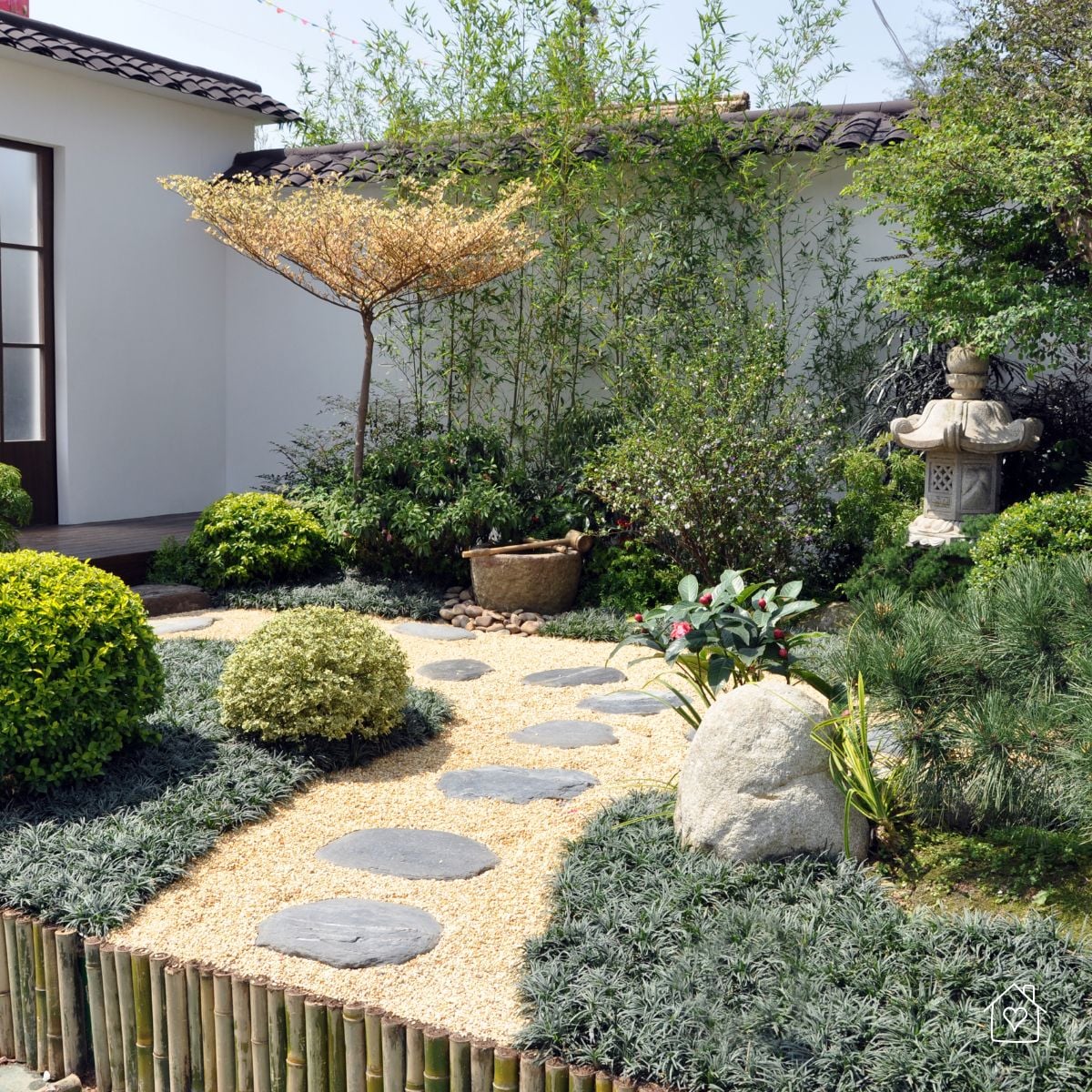 Small Japanese garden courtyard with curved stepping-stone path, stone lantern, bamboo backdrop, and mossy groundcovers.