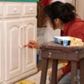 DIYer painting cabinet doors with a small brush to refresh old furniture with white paint.