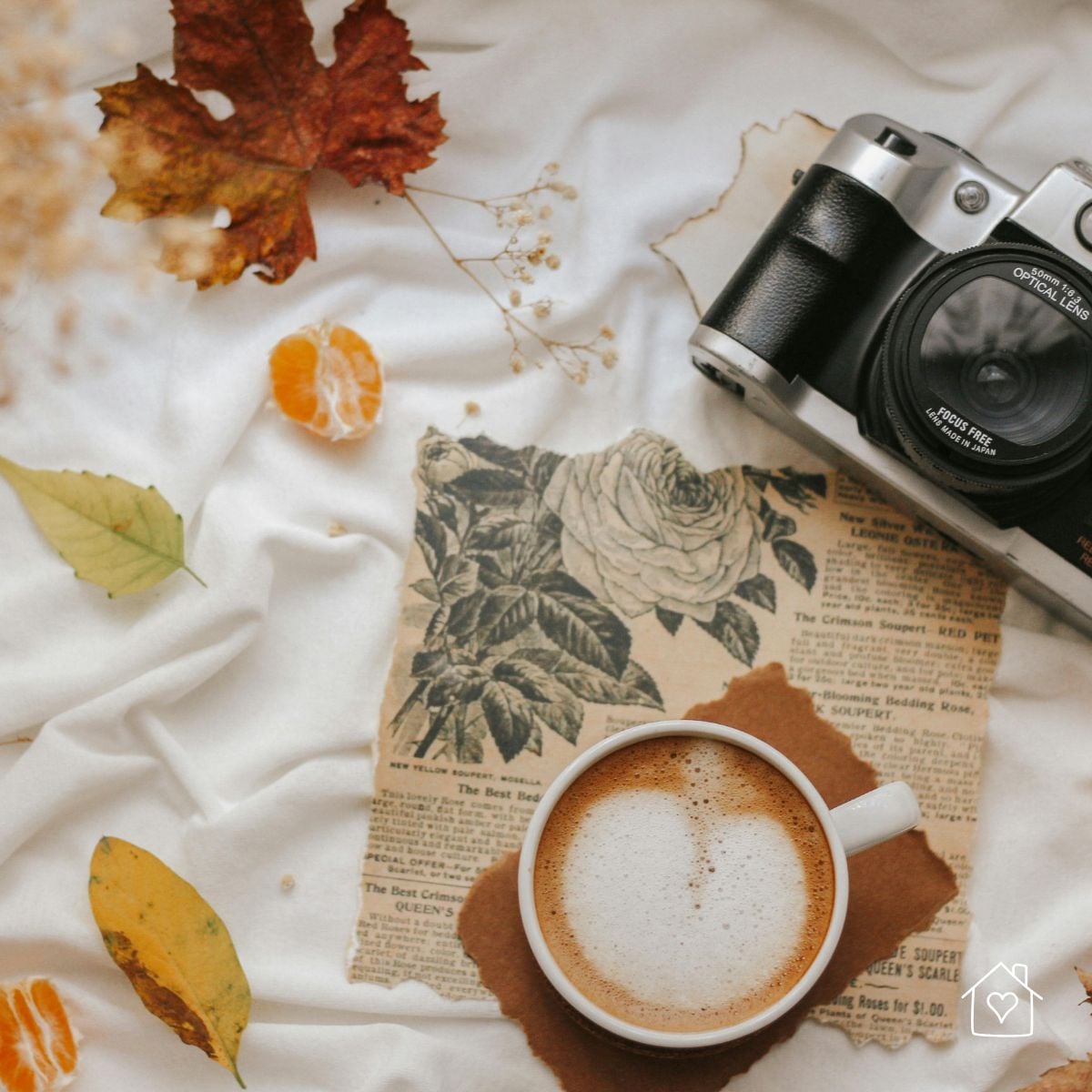 Flat lay with vintage-style camera, latte, pressed leaves, and torn paper ephemera.