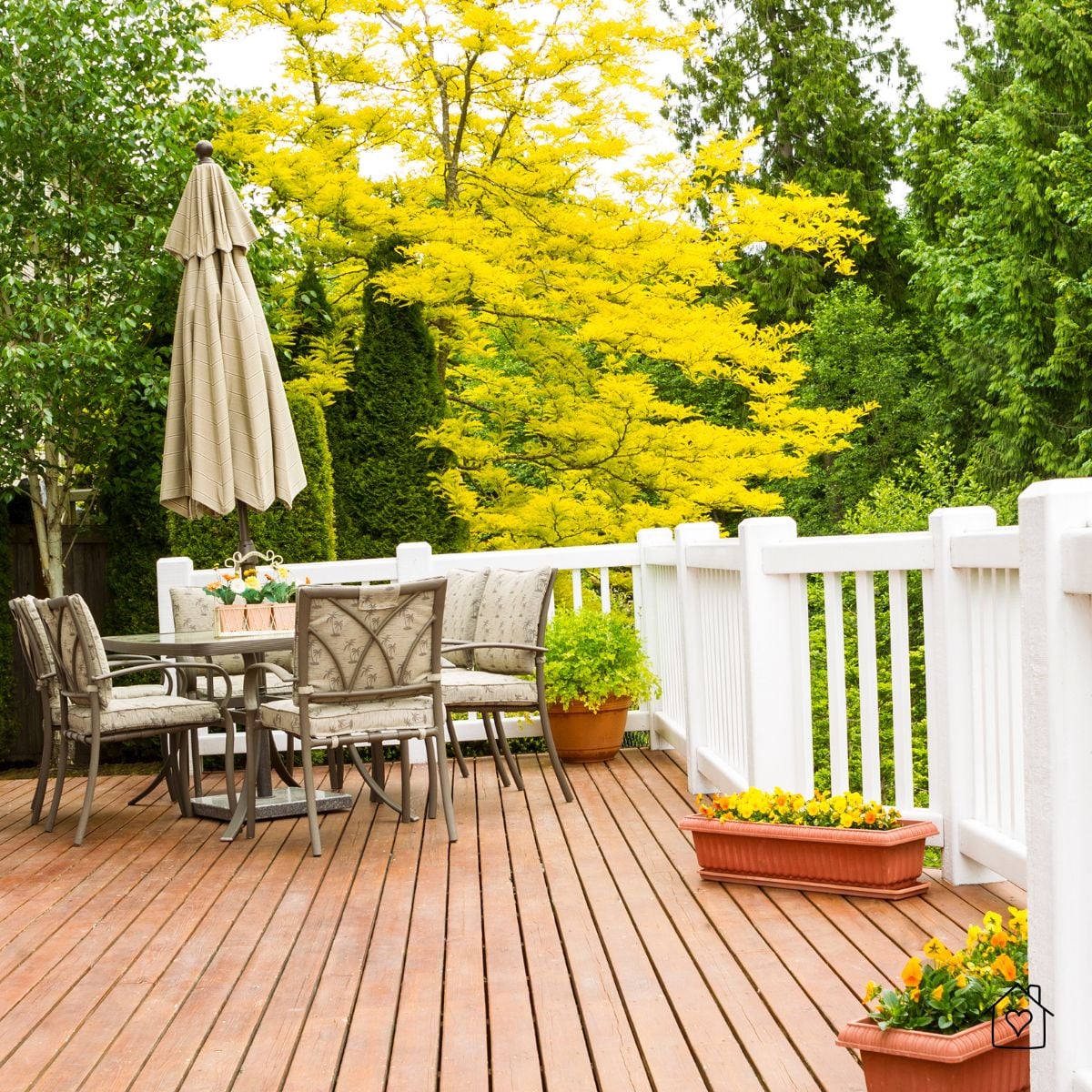 backyard deck with patio table, umbrella, white railing, and flowering planters