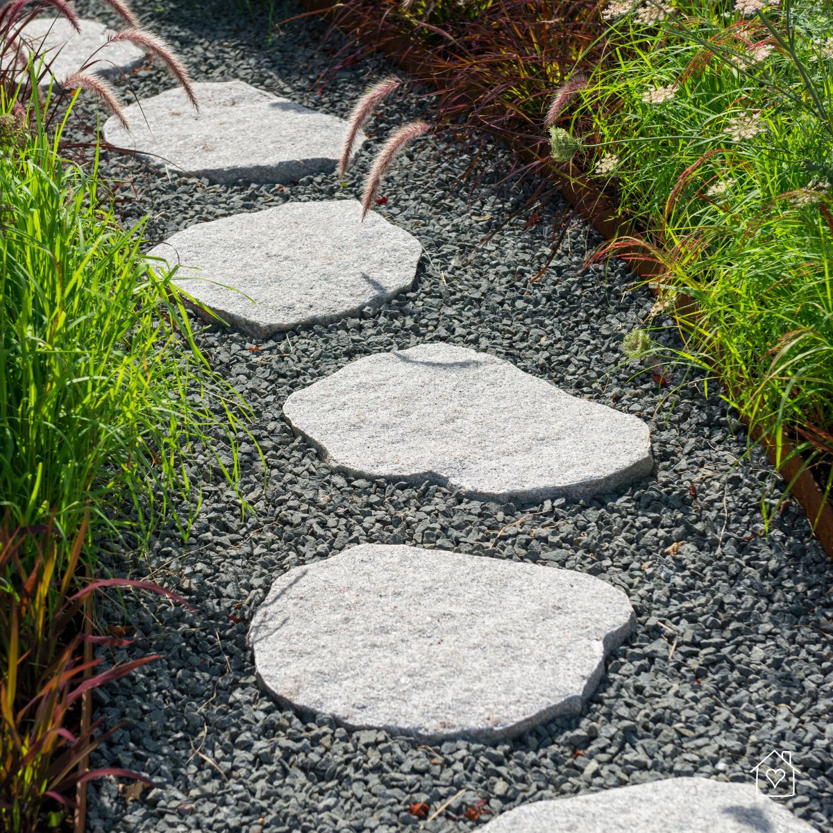 Close view of irregular stone pavers set in dark gravel with edging and ornamental grasses