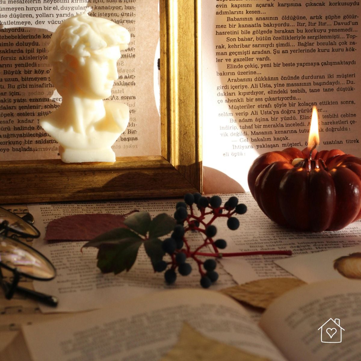 Close-up of a styled vignette featuring a classical bust, candle, berries, and framed book page.