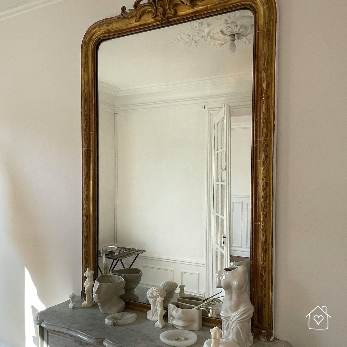 Antique gold mirror above a marble mantel with sculptural decor.