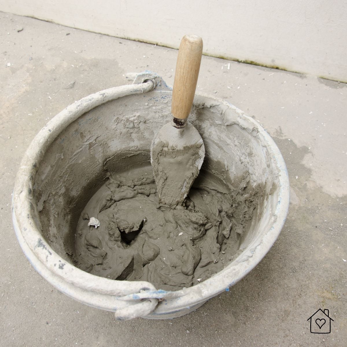 Bucket of ready-mixed fire cement with a trowel, showing thick, workable consistency for sealing firebrick and flue joints.
