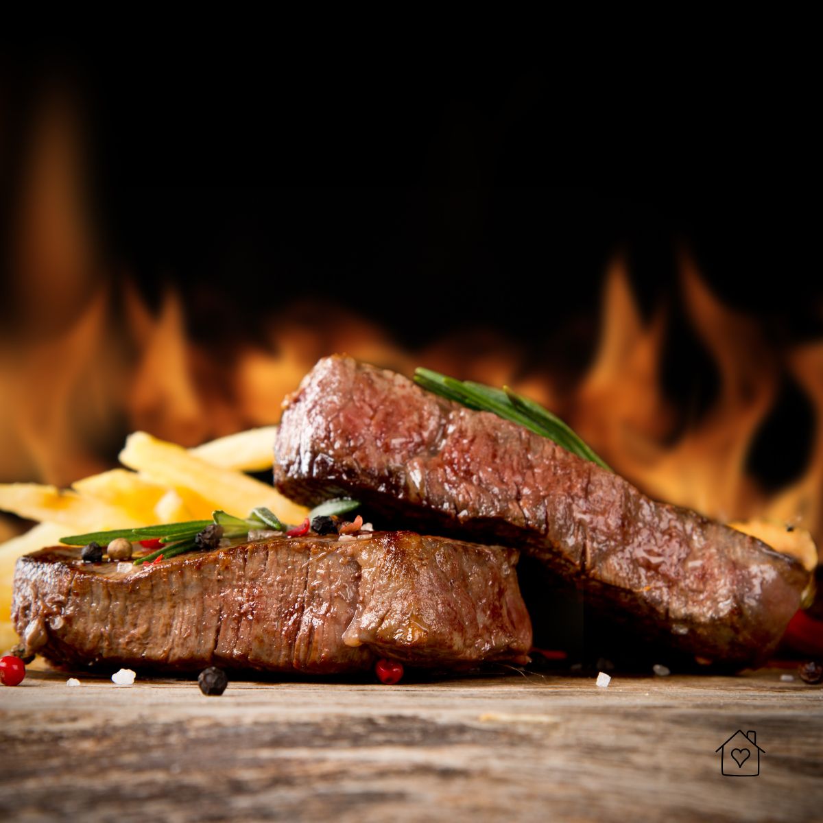 Two flame-seared steaks resting with peppercorns and sea salt, fire in the background