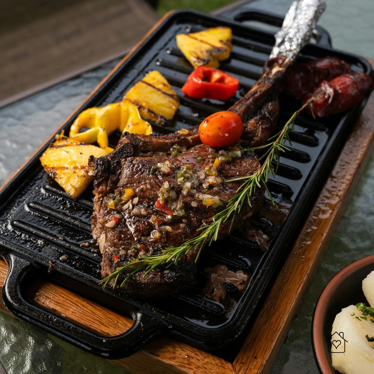 Tomahawk ribeye seared on a cast-iron grill pan with rosemary, peppers, and pineapple slices