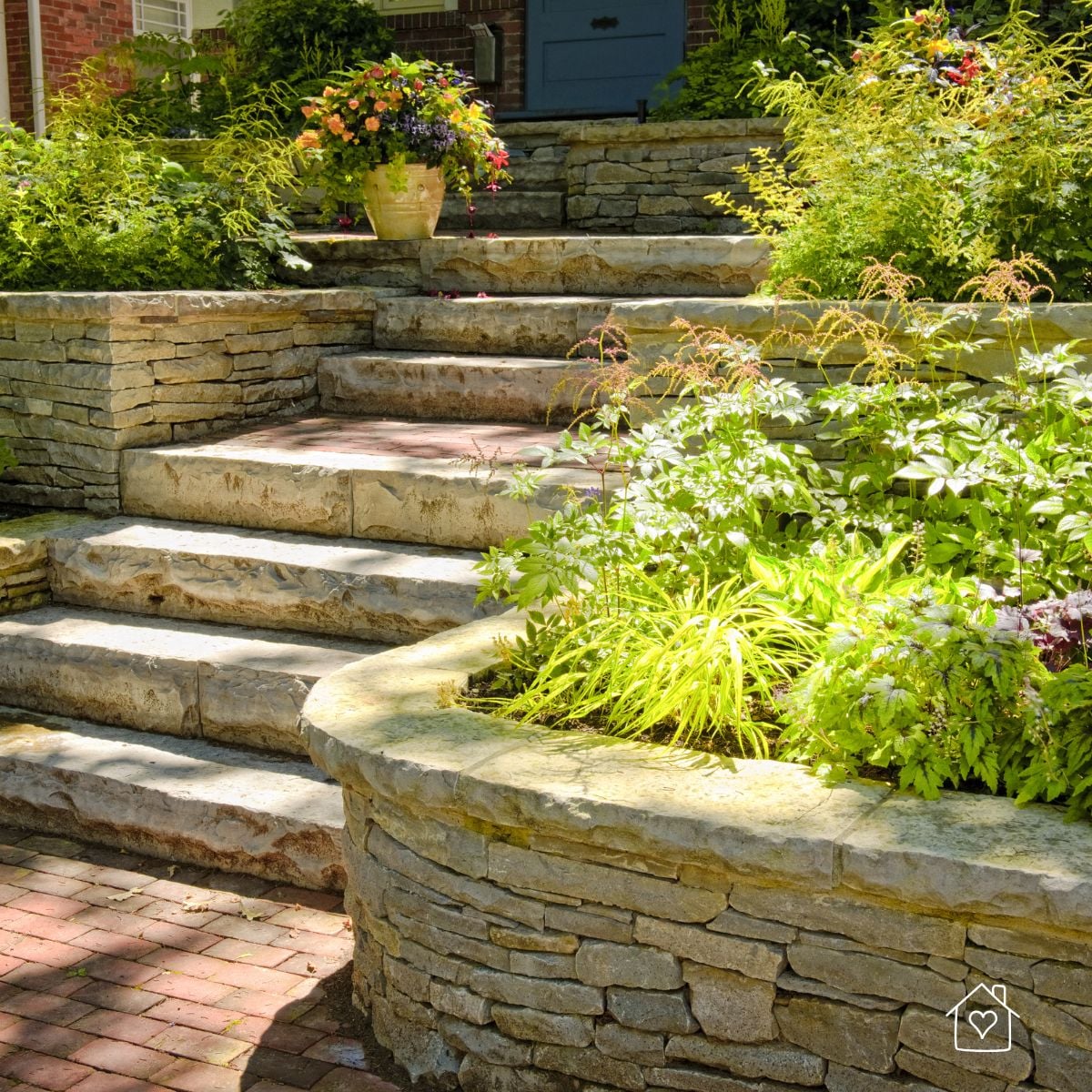 Stone garden steps with stacked-stone retaining walls and leafy plantings leading up to a front entry.