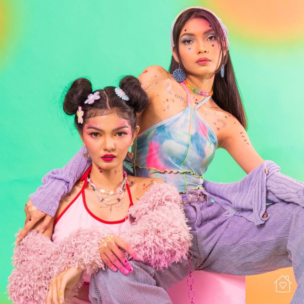 two women in colorful Y2K outfits with playful stickers posing against a bright backdrop for a retro home photoshoot