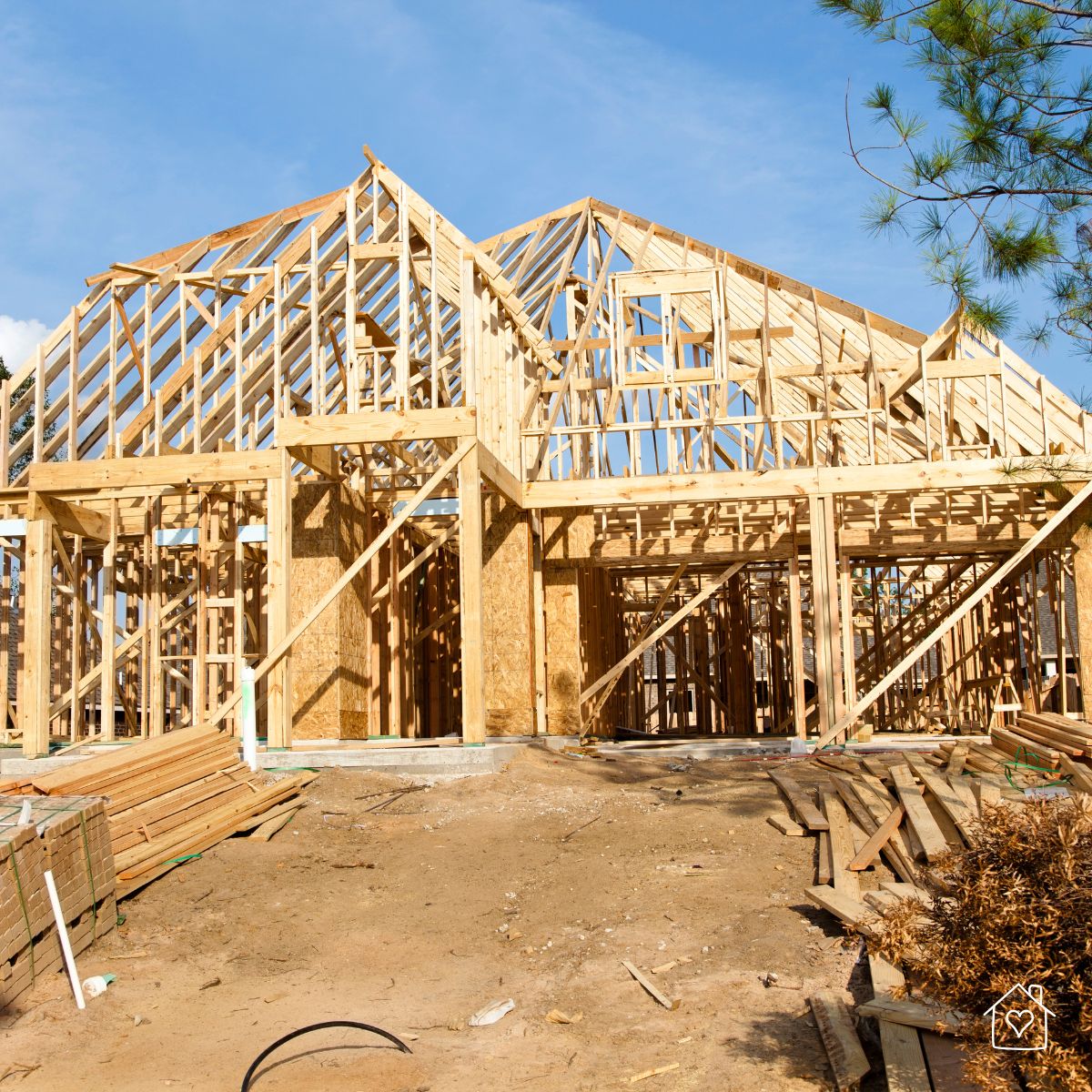 New home construction framing phase showing roof trusses, studs, and building materials onsite.