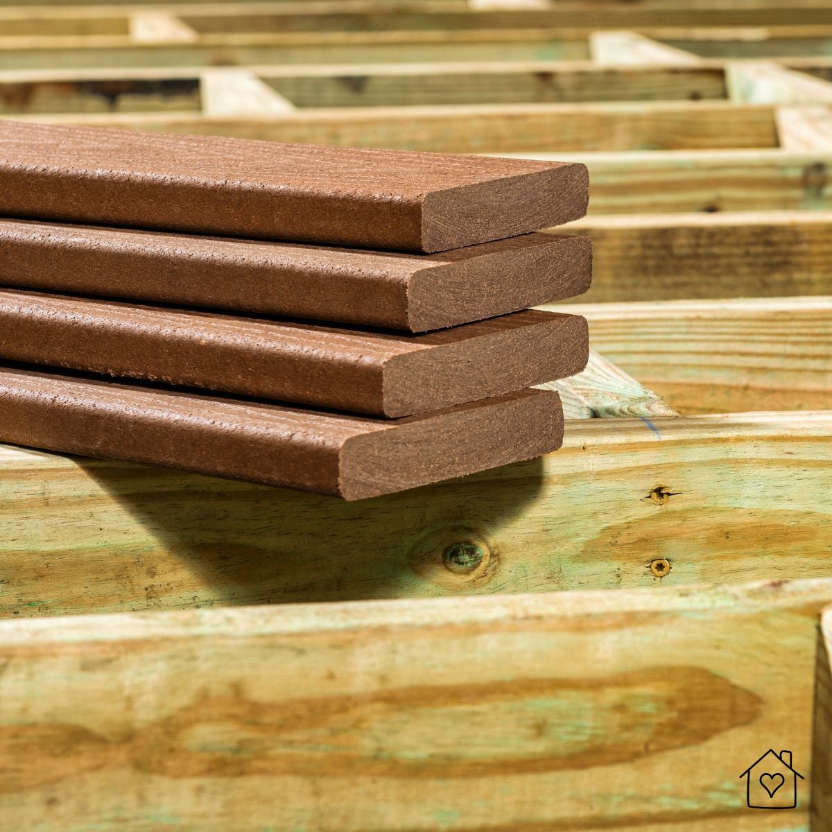 Brown composite deck boards stacked on pressure-treated lumber joists, showing typical substructure.