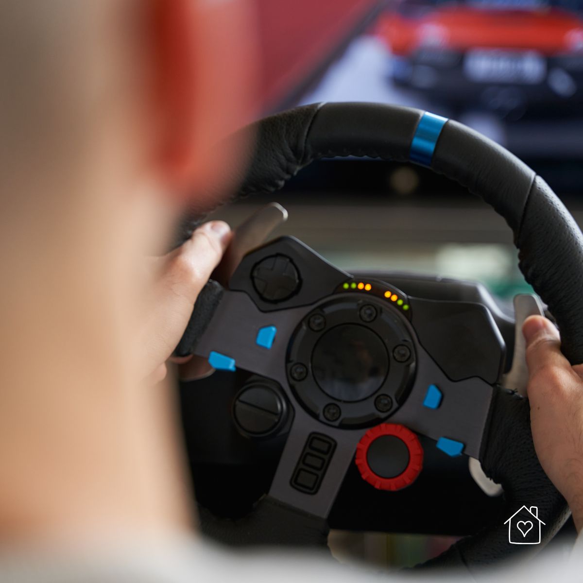 Close-up of a person holding a racing simulator steering wheel with LED rev lights, in front of a blurred racing game screen.