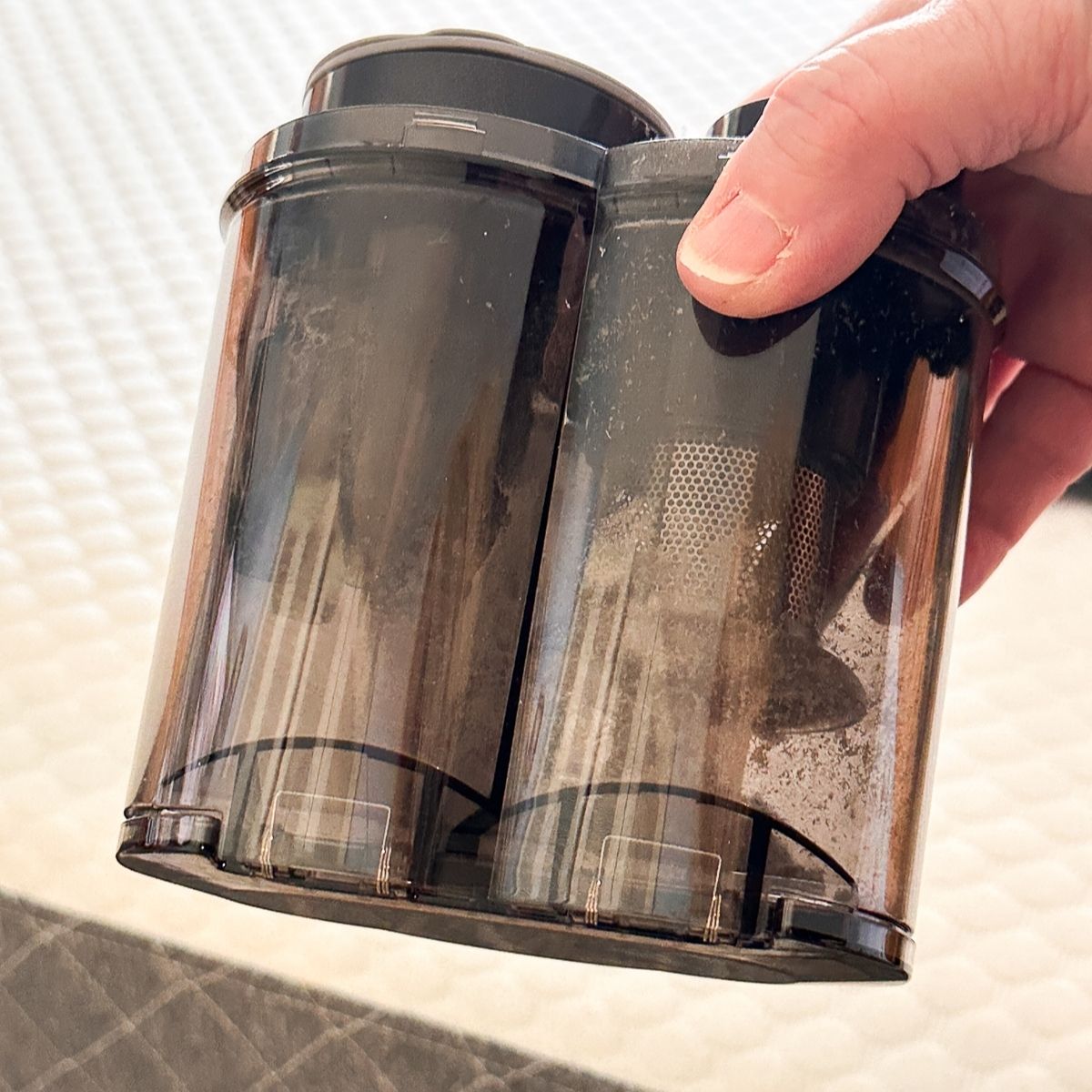 Two detached cylindrical dust collection chambers from the FEPPO mattress vacuum, showing accumulated dirt and debris through the transparent walls
