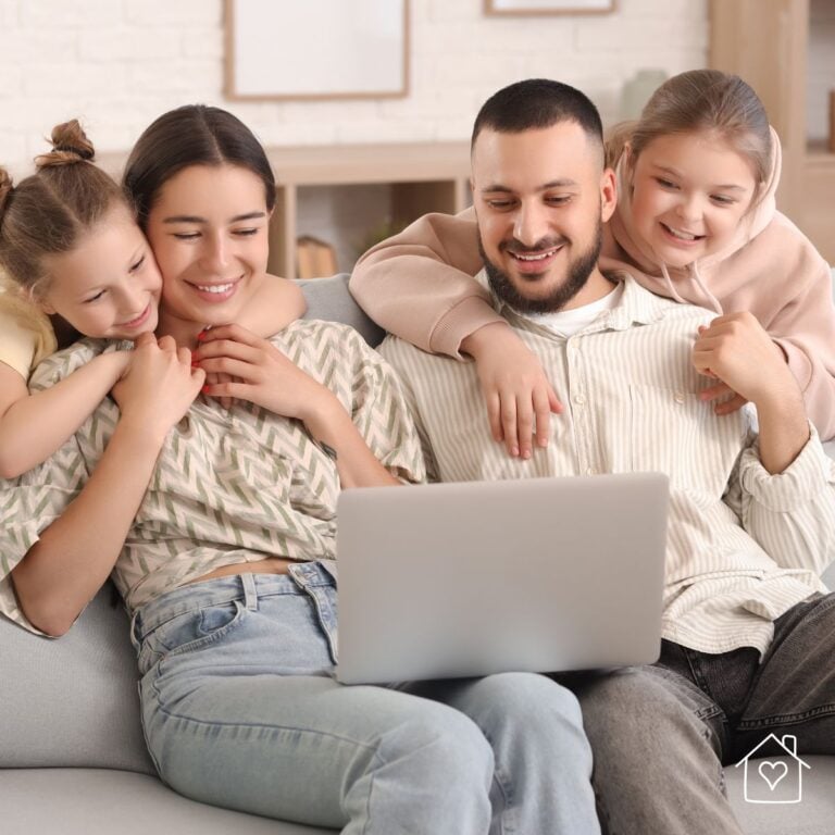 Parents and two children sitting on a couch looking at a laptop while reviewing family photos to print for albums or home decor