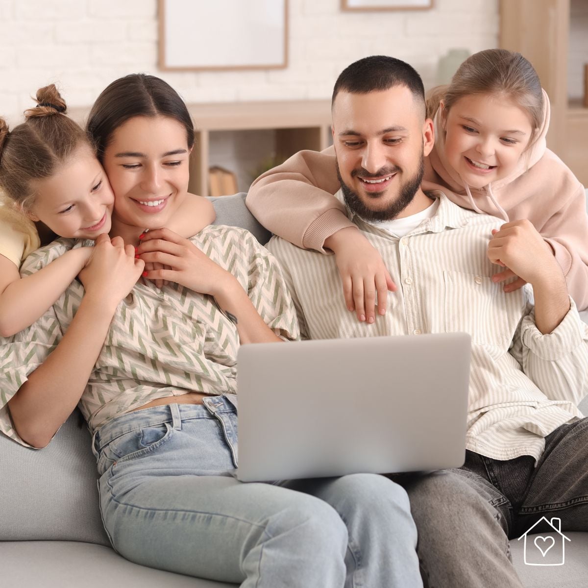 Parents and two children sitting on a couch looking at a laptop while reviewing family photos to print for albums or home decor