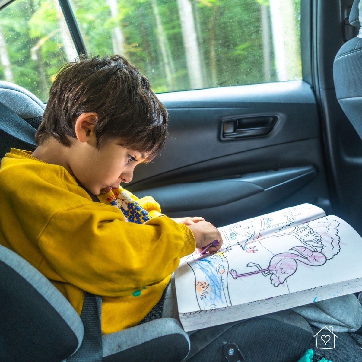 Young child sitting buckled in a car seat and coloring in a book during a car ride.