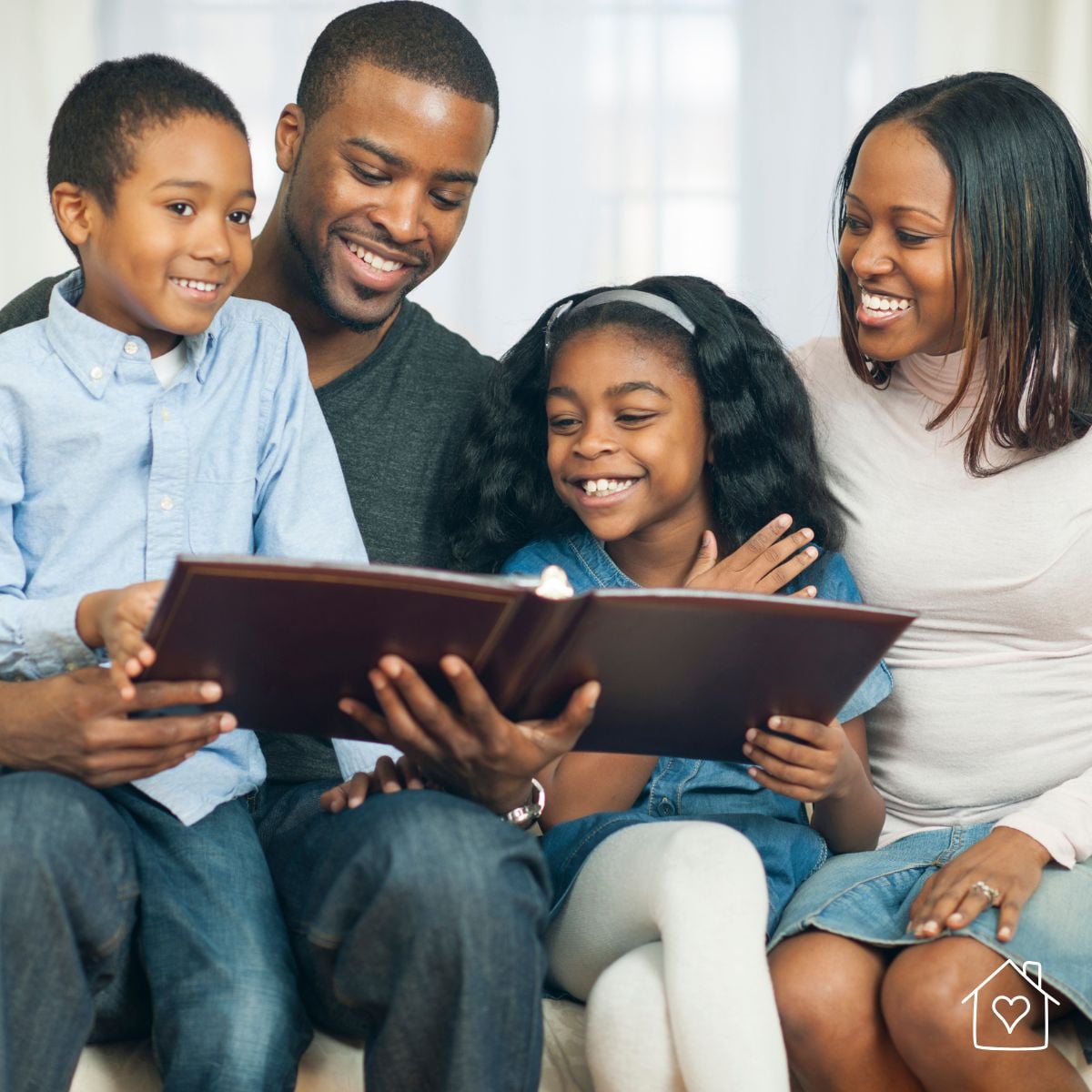 Smiling family sitting together and looking through a photo album, representing printed family memories for albums and home display