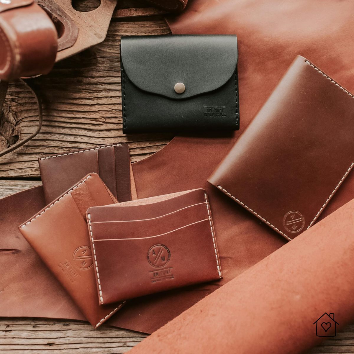 Handmade leather wallets, card holders, and a small coin pouch arranged on leather hides and wood.