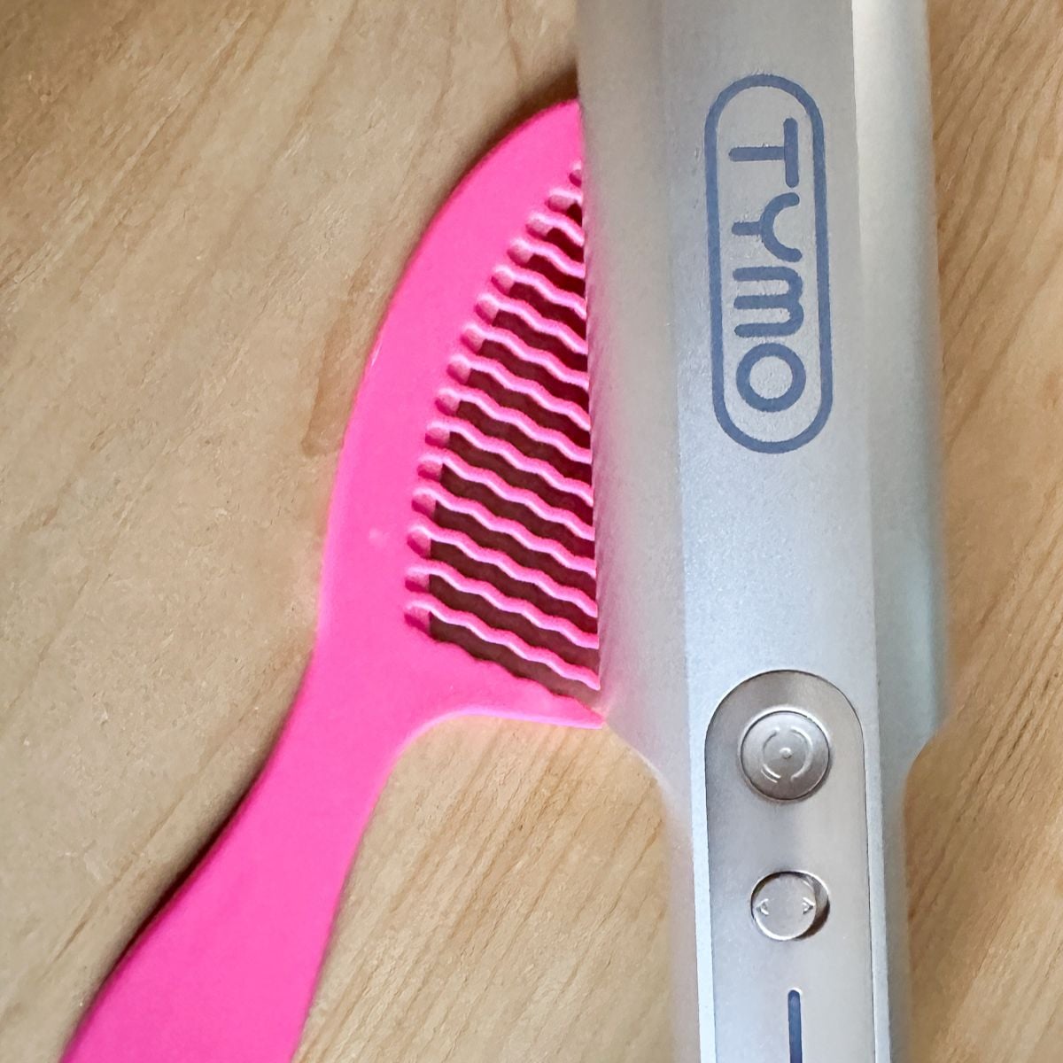 TYMO CurlPro automatic rotating curling iron in pink next to a styling comb on a wood surface