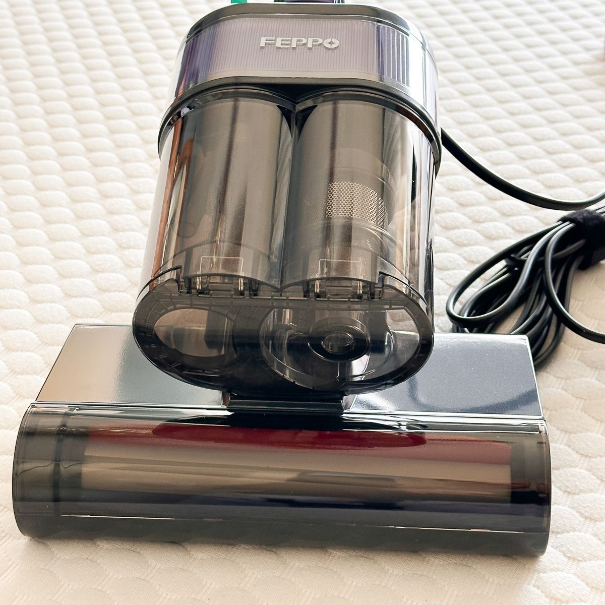 The FEPPO mattress vacuum cleaner sitting upright on a white mattress, showing its dual-cylinder dust collection chamber and rolling brush head