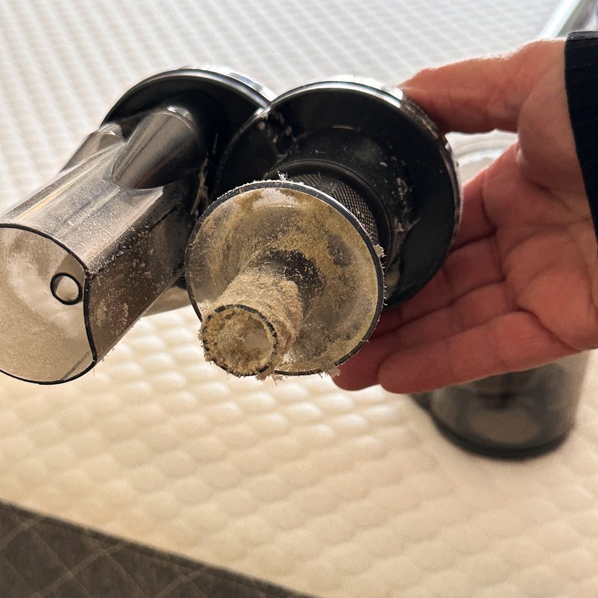 A hand holding the opened FEPPO vacuum filter assembly showing a cylindrical filter heavily coated in fine dust and debris