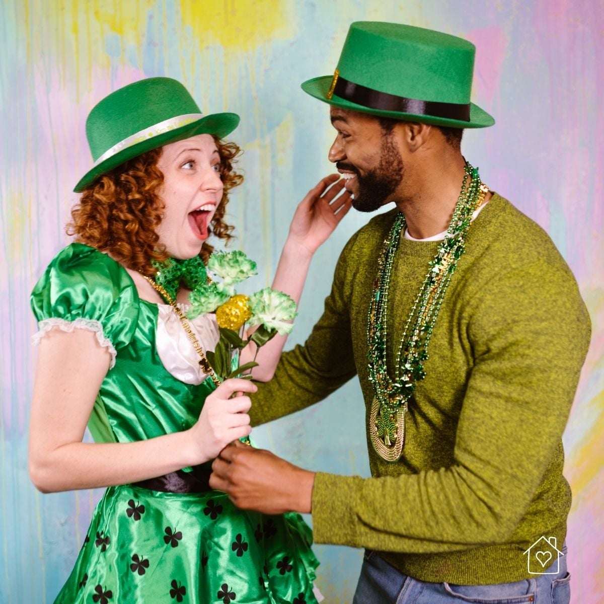 Woman with red hair in a cute St. Patrick's costume skirt and blouse with a green hat standing next to a smiling man wearing a green St. Patrick's Day hat and necklaces