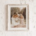 8x10 white distressed frame featuring a warm outdoor portrait of a mother with two young children against a textured white wall.