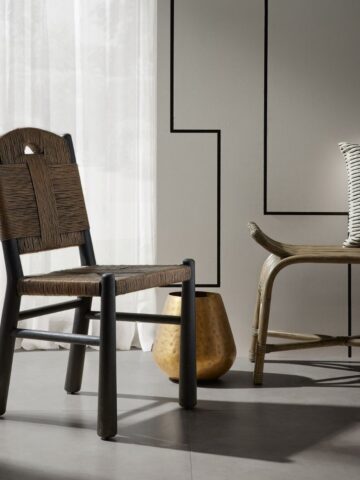 High end woven dining chair with black wood legs in a modern neutral dining room beside a rattan bench and sheer white curtains