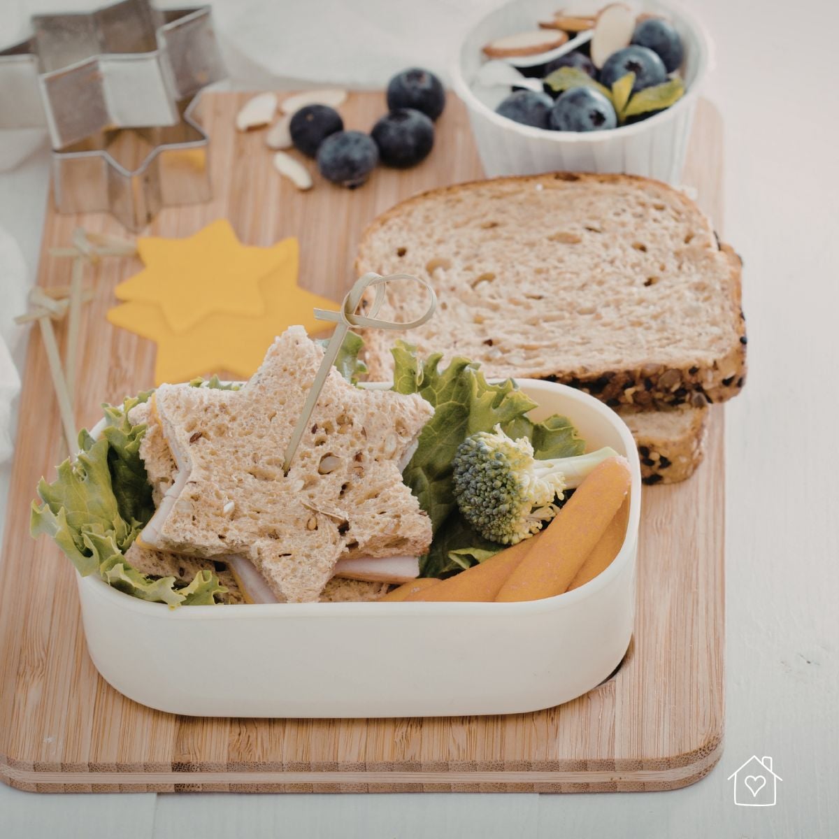 Lunchbox with a star-shaped mini sandwich, lettuce, carrots, broccoli, blueberries, almonds, and whole grain bread.