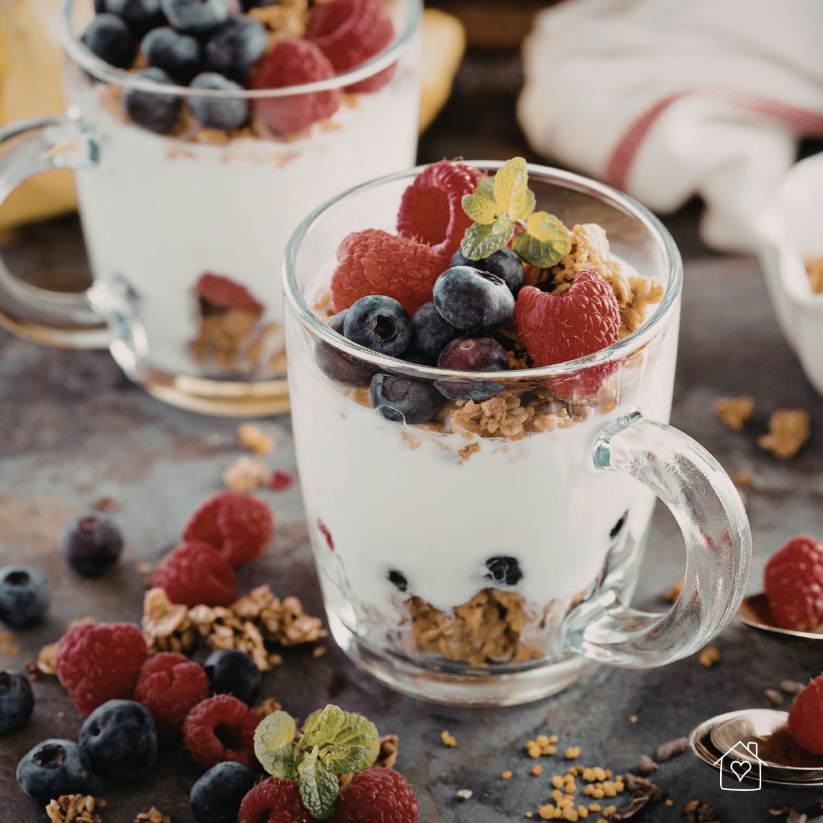 Glass cups of yogurt parfait topped with blueberries, raspberries, granola, and mint for an easy school lunch snack.