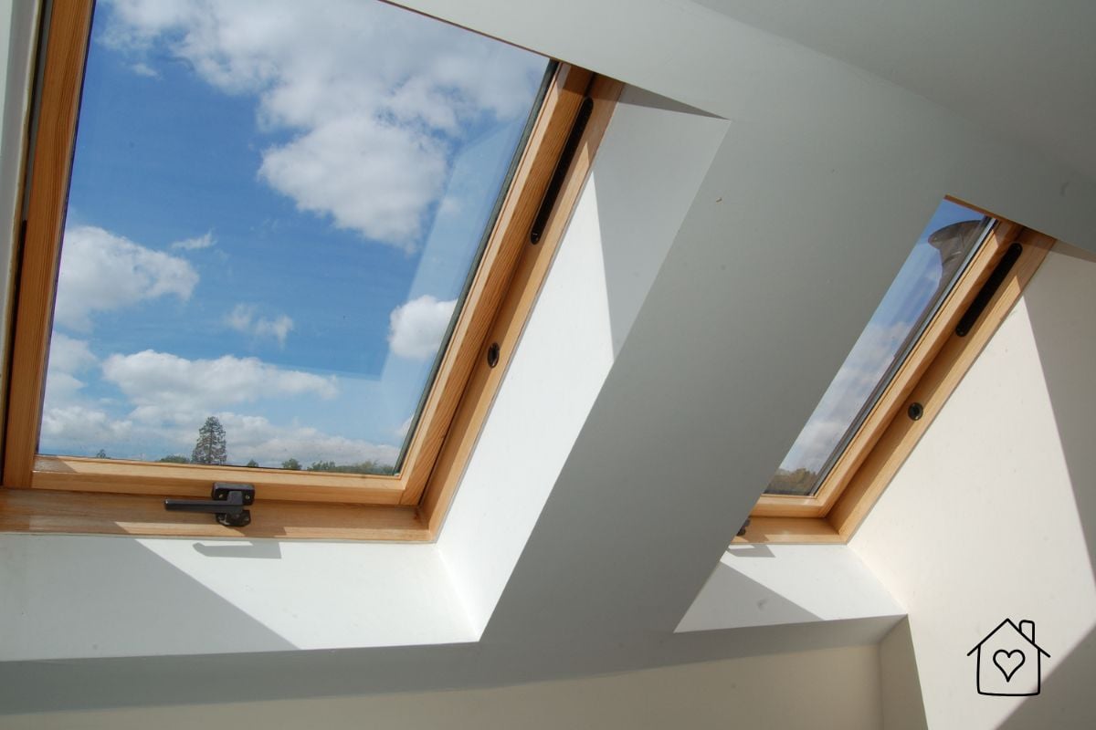 Two timber-framed roof windows set into a white ceiling with blue sky visible above