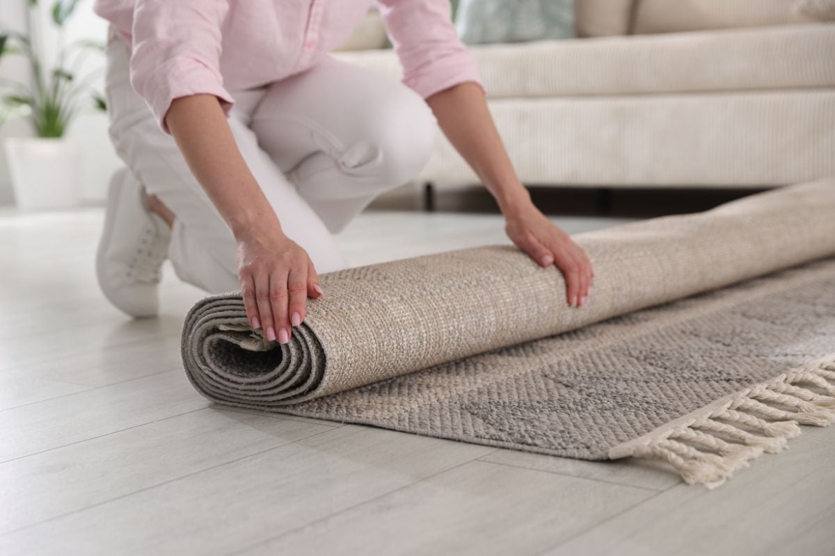 Person rolling out a textured beige rug with fringe on a light floor in a neutral living room