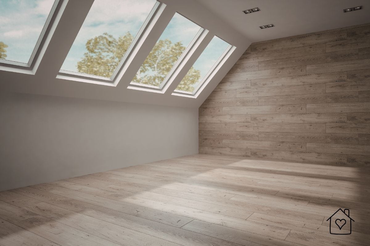 Empty loft room with pale wood flooring, timber feature wall, and multiple roof windows filling the space with daylight