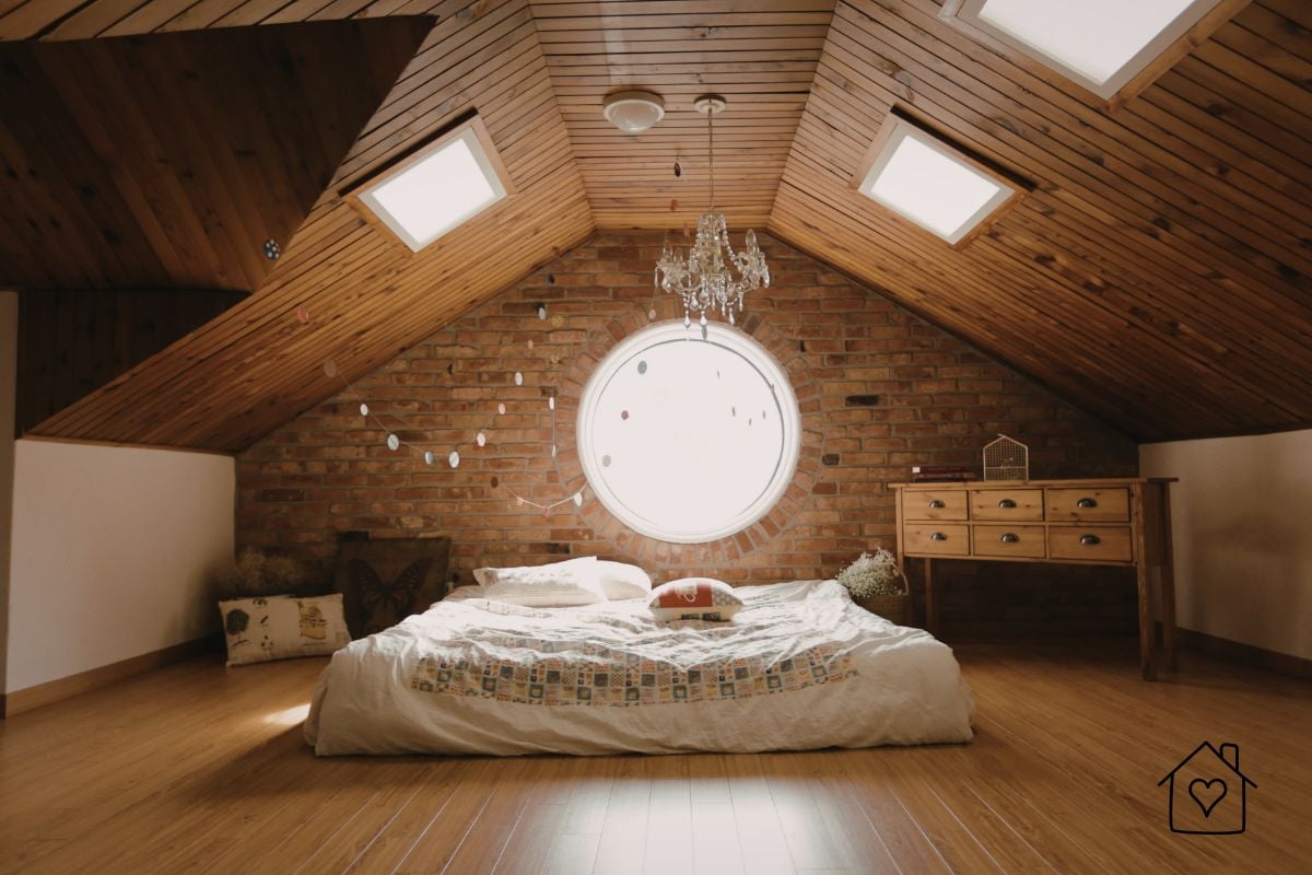 Cosy loft bedroom with timber-panelled ceiling, circular window, and skylights adding natural light