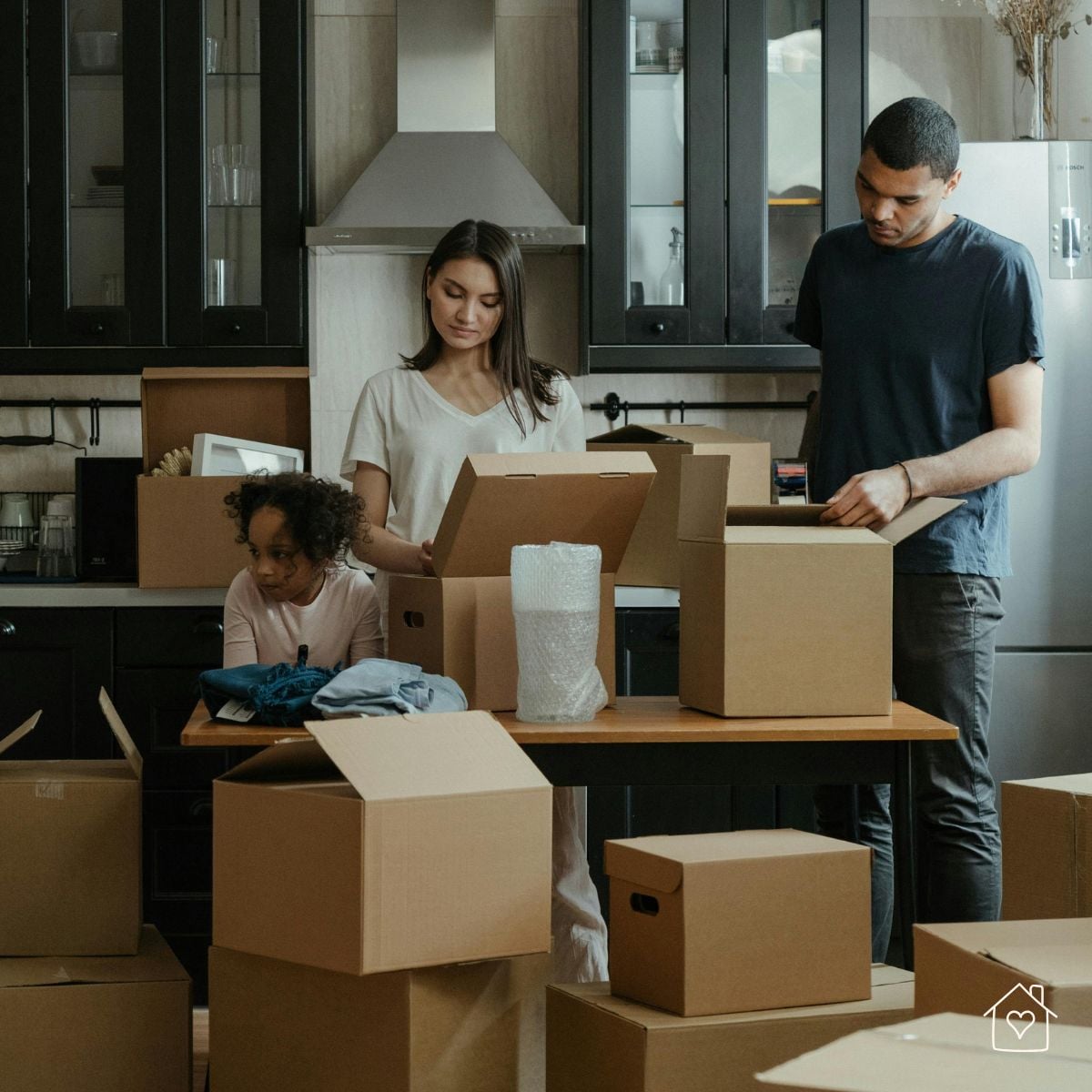 Family packing dishes and household items in moving boxes in a kitchen