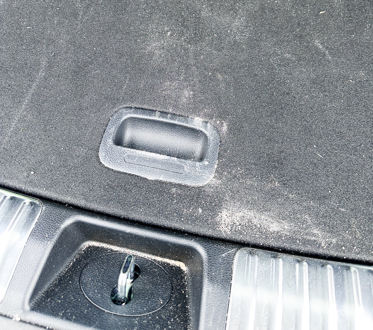 Dirty black car cargo area with sand and debris before cleaning with the FEPPO cordless vacuum.