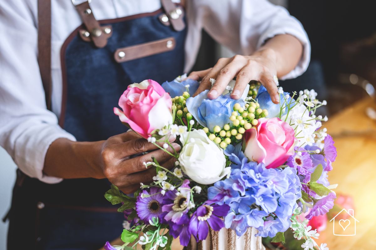 Florist arranging pink, blue, white, and purple flowers into a fresh bouquet for an event or floral display