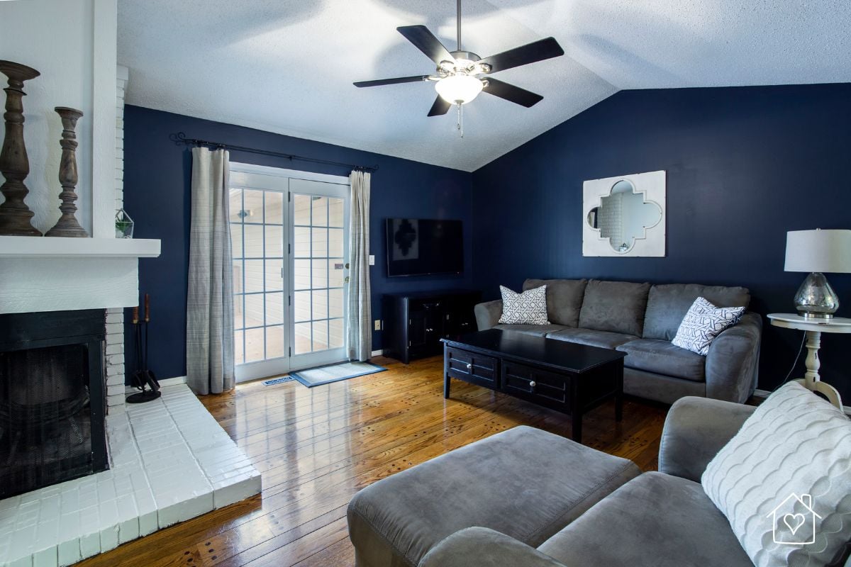 Black five blade ceiling fan with a light installed in a navy blue living room with a fireplace and hardwood floors.