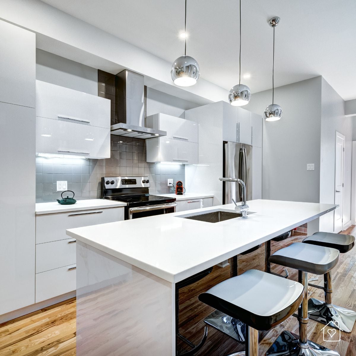 Modern white apartment kitchen with an island, bar stools, stainless steel appliances, and pendant lights.
