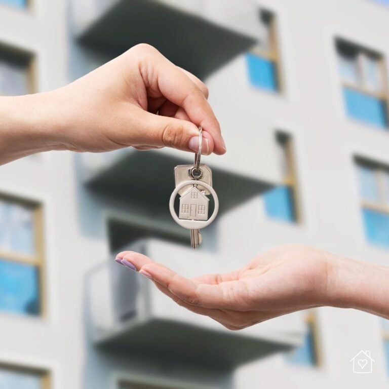 One person handing apartment keys to another in front of a residential building.