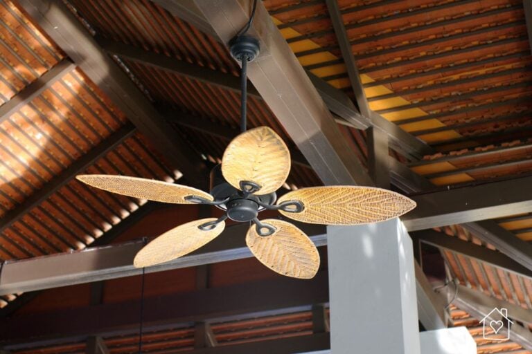 Tropical ceiling fan with woven leaf shaped blades hanging from a high exposed beam ceiling.