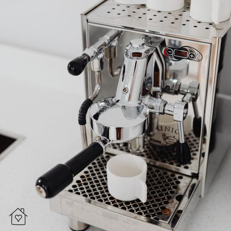 Stainless steel heat exchanger espresso machine with dual portafilter handles pulling a shot into a white cup on a kitchen counter