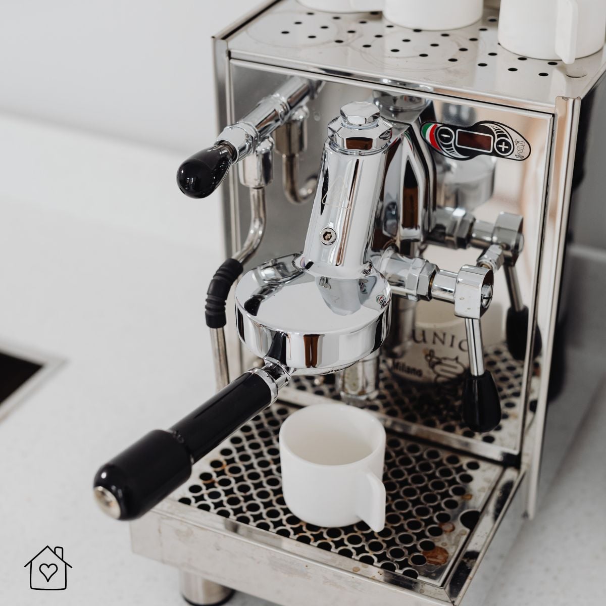 Stainless steel heat exchanger espresso machine with dual portafilter handles pulling a shot into a white cup on a kitchen counter