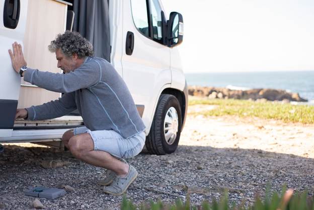Man crouching beside a caravan while completing safety and maintenance checks before traveling.For the strongest SEO and accessibility, I kept the alt text natural and descriptive rather than stuffing it with every caravan-maintenance keyword.