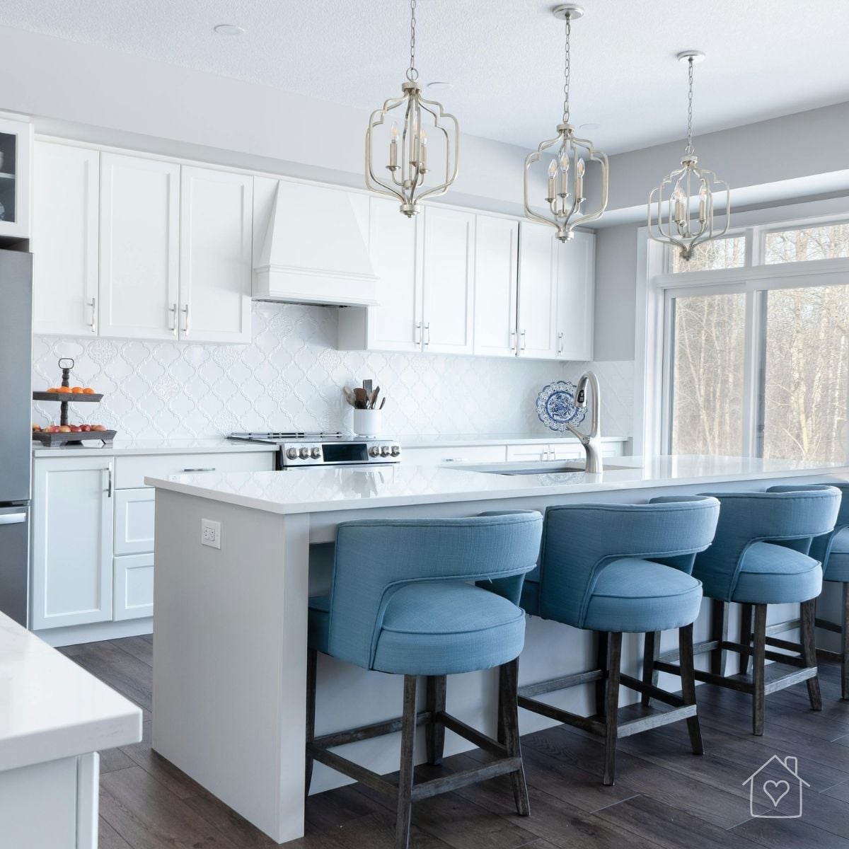 Bright white remodeled kitchen with a large island, blue counter stools, pendant lights, and floor-to-ceiling windows