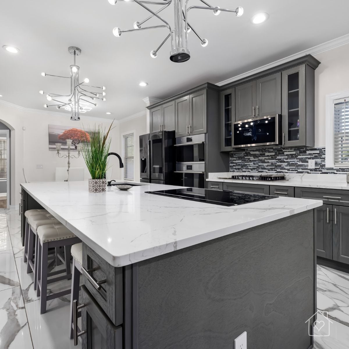 Modern gray kitchen with an oversized white quartz island, black appliances, contemporary lighting, and counter seating