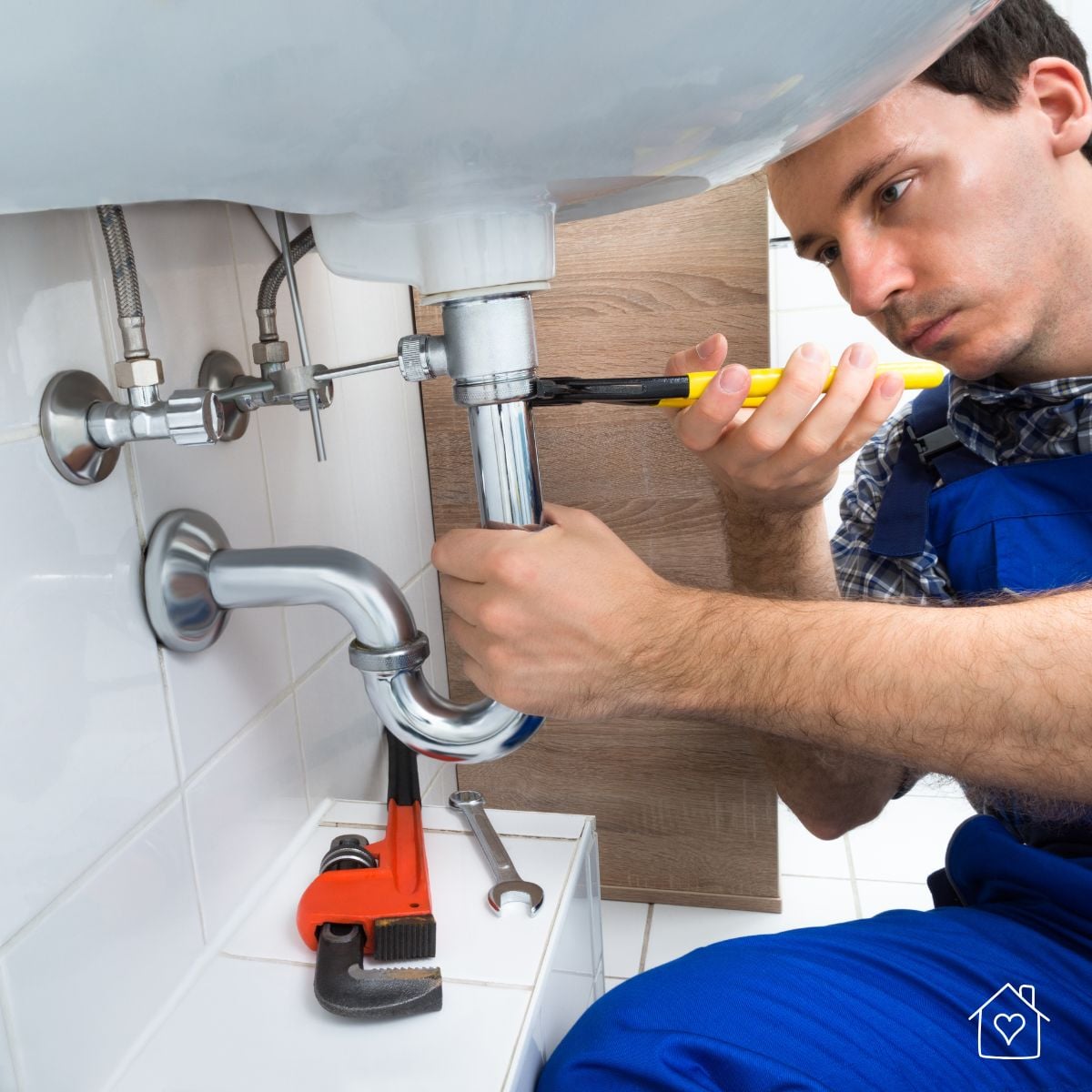 Plumber in blue overalls using pliers to repair the P-trap pipe under a bathroom sink
