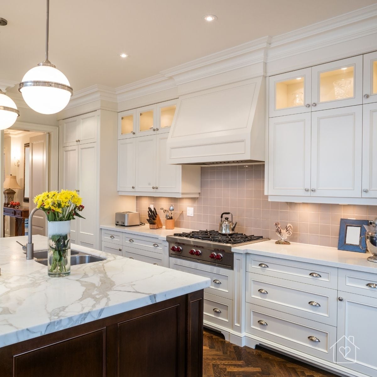 Traditional white kitchen with a marble-topped island, pendant lighting, custom cabinets, and a built-in range hood