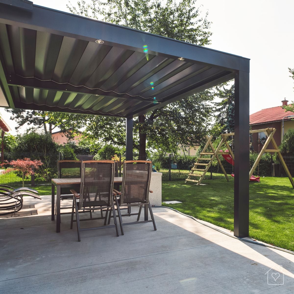 A modern aluminum pergola shades an outdoor dining set on a patio, with a green lawn and kids play area in the background