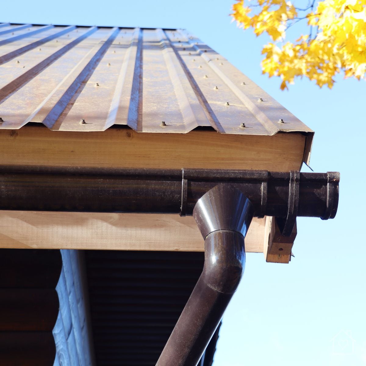 A close up view of a rain gutter and downspout tucked beneath a covered roof edge